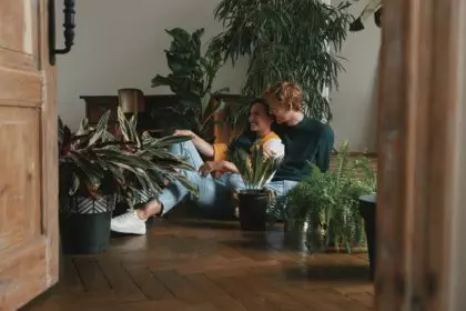 Beautiful young couple watering houseplants while sitting on the floor at home