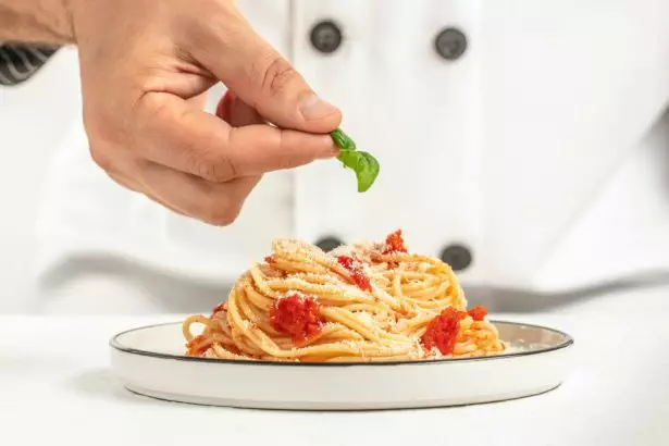 Chef preparing delicious pasta tomatoes and basil on a light background. Italian cuisine