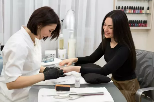 Woman in a nail salon receiving a manicure by a beautician with nail file.