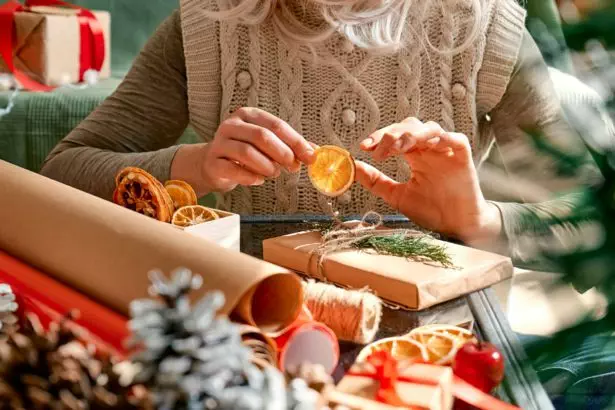Woman wrapping presents in recycled card and decorated it with dried oranges and fir branches.