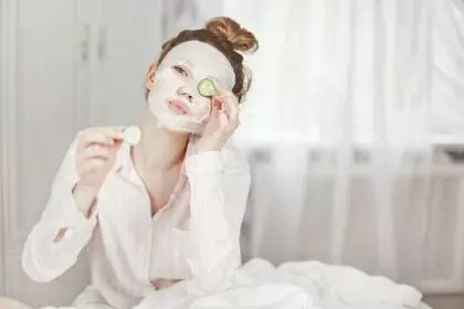 A cute girl with a face mask covers one eye with a slice of cucumber