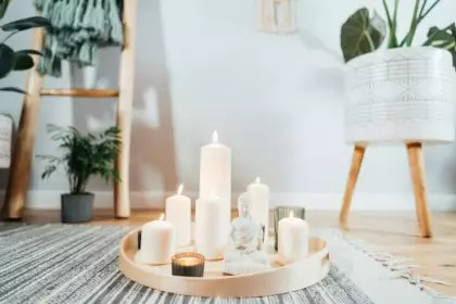 Wooden tray with burning candles and white Buddha statuette on the floor of modern interior.
