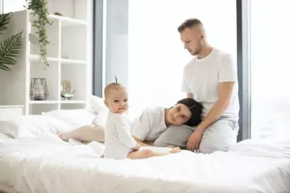 Kid sitting on bed near parents at home in morning