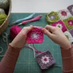 Girl's hands crochetting with colorful yarn granny squares blanket. Hobby crafting and handmade