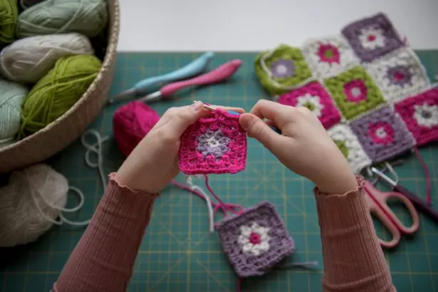 Girl's hands crochetting with colorful yarn granny squares blanket. Hobby crafting and handmade