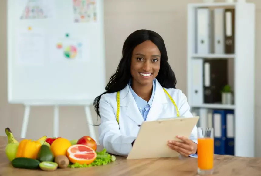 Positive black nutritionist with clipboard creating healthy meal plan for patient at clinic, blank
